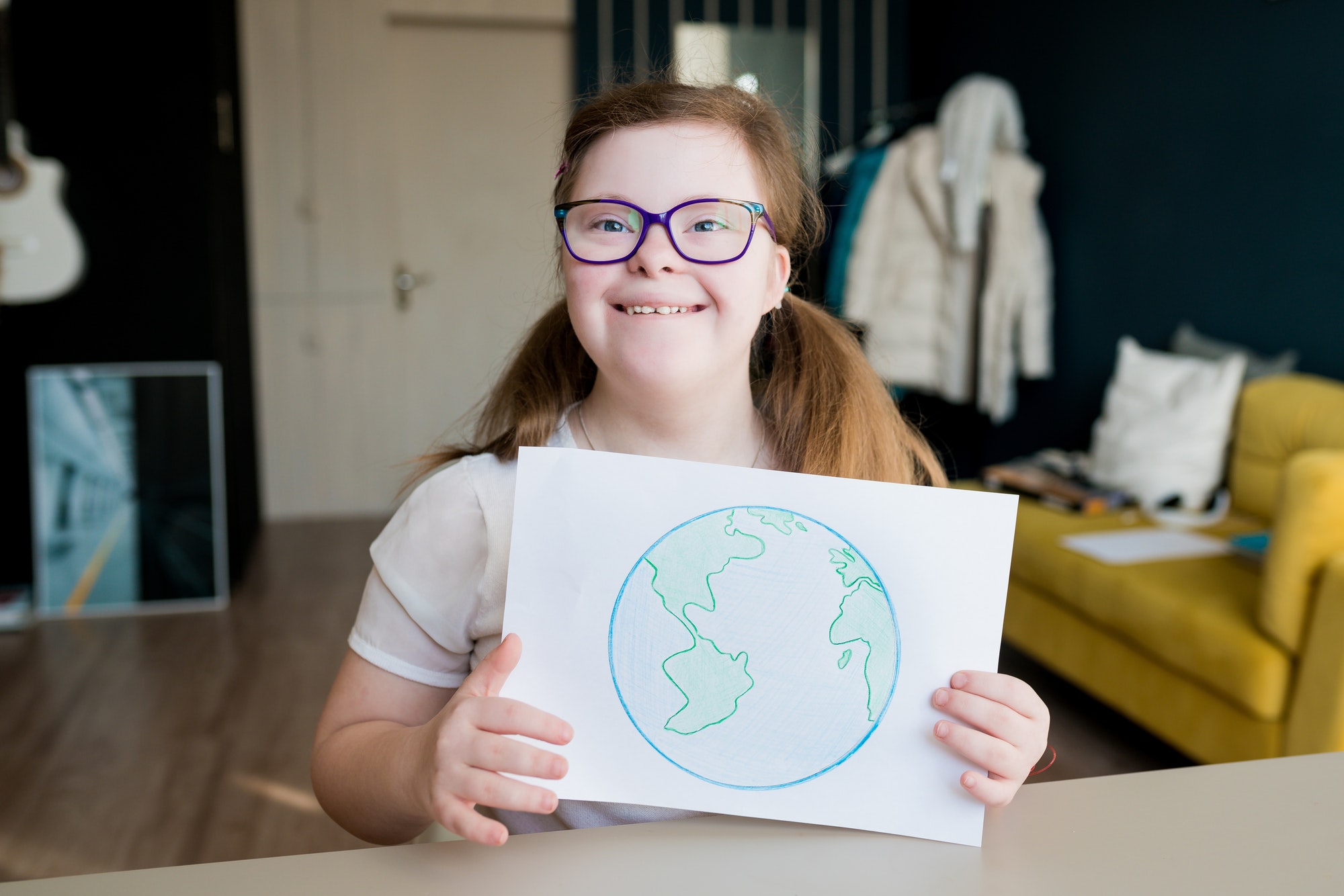 Teenage girl with Down syndrome holding drawing of the planet Earth at home